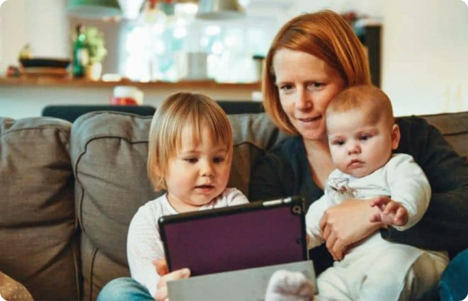 A woman and two children sitting on a couch, engrossed in a tablet.